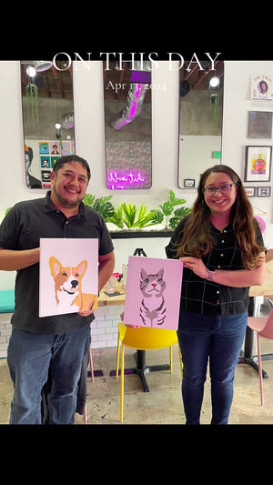 Two people holding up paintings of a dog and a cat in an art studio.