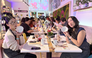 Two women sitting at a table in a colorful indoor setting, possibly a cafe or event space, with various items on the table.